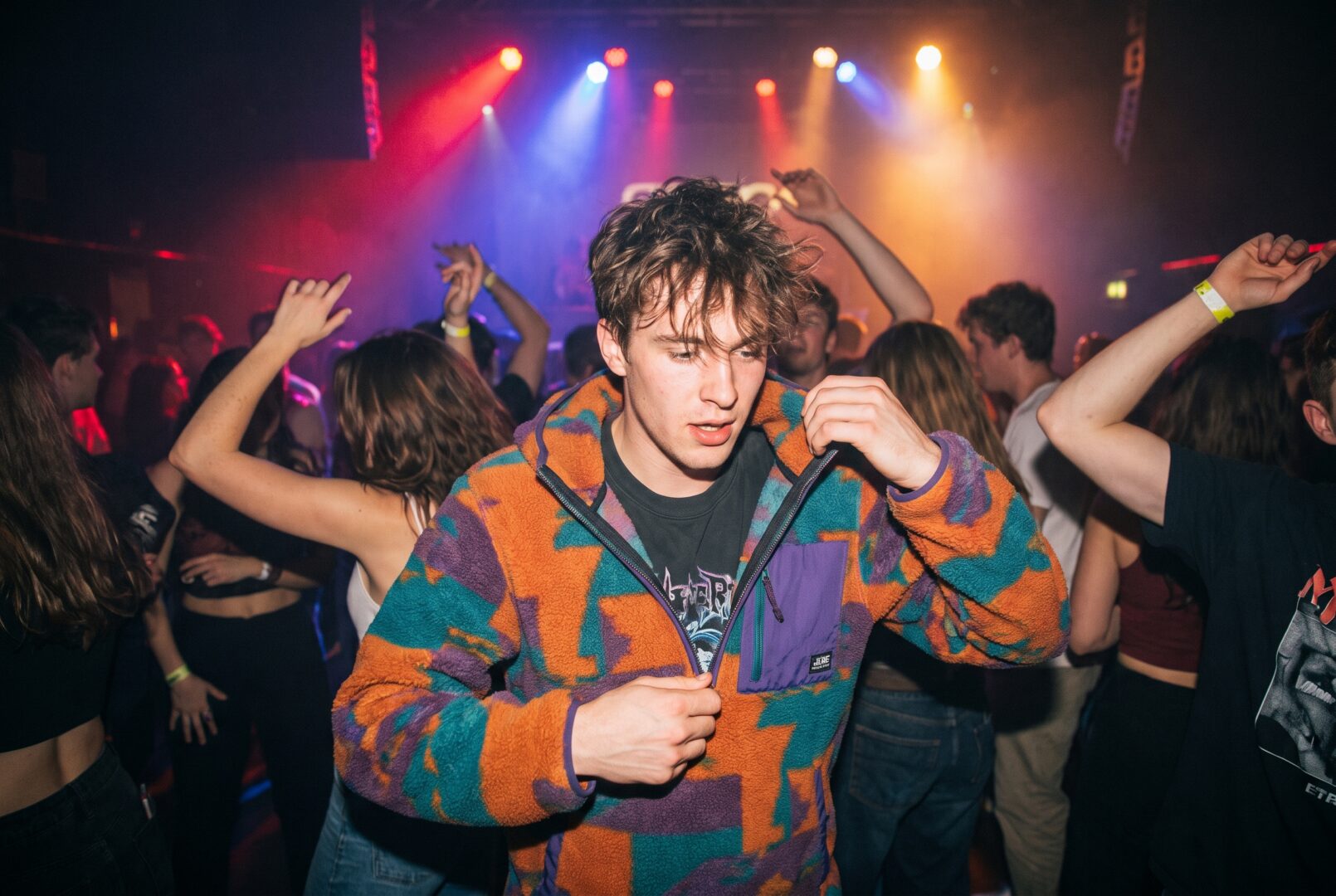 Man in a zip-up hoodie over a tee in a club crowd