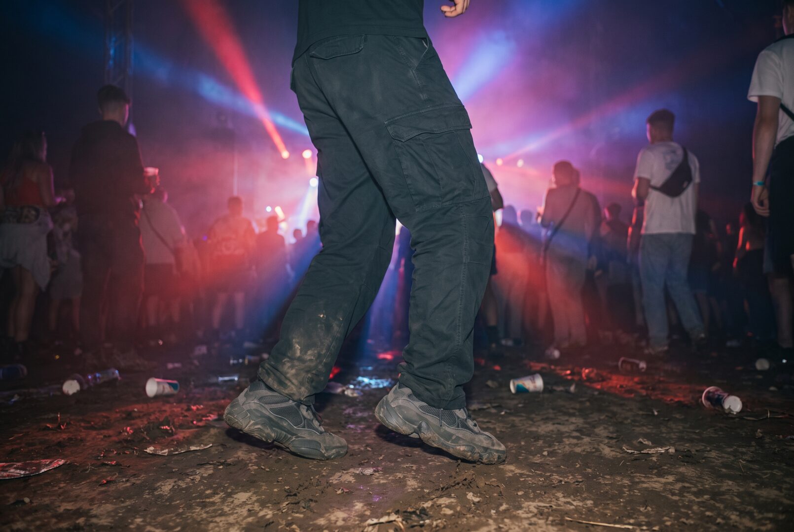 Man in dark cargo trousers and worn trainers dancing at a rave