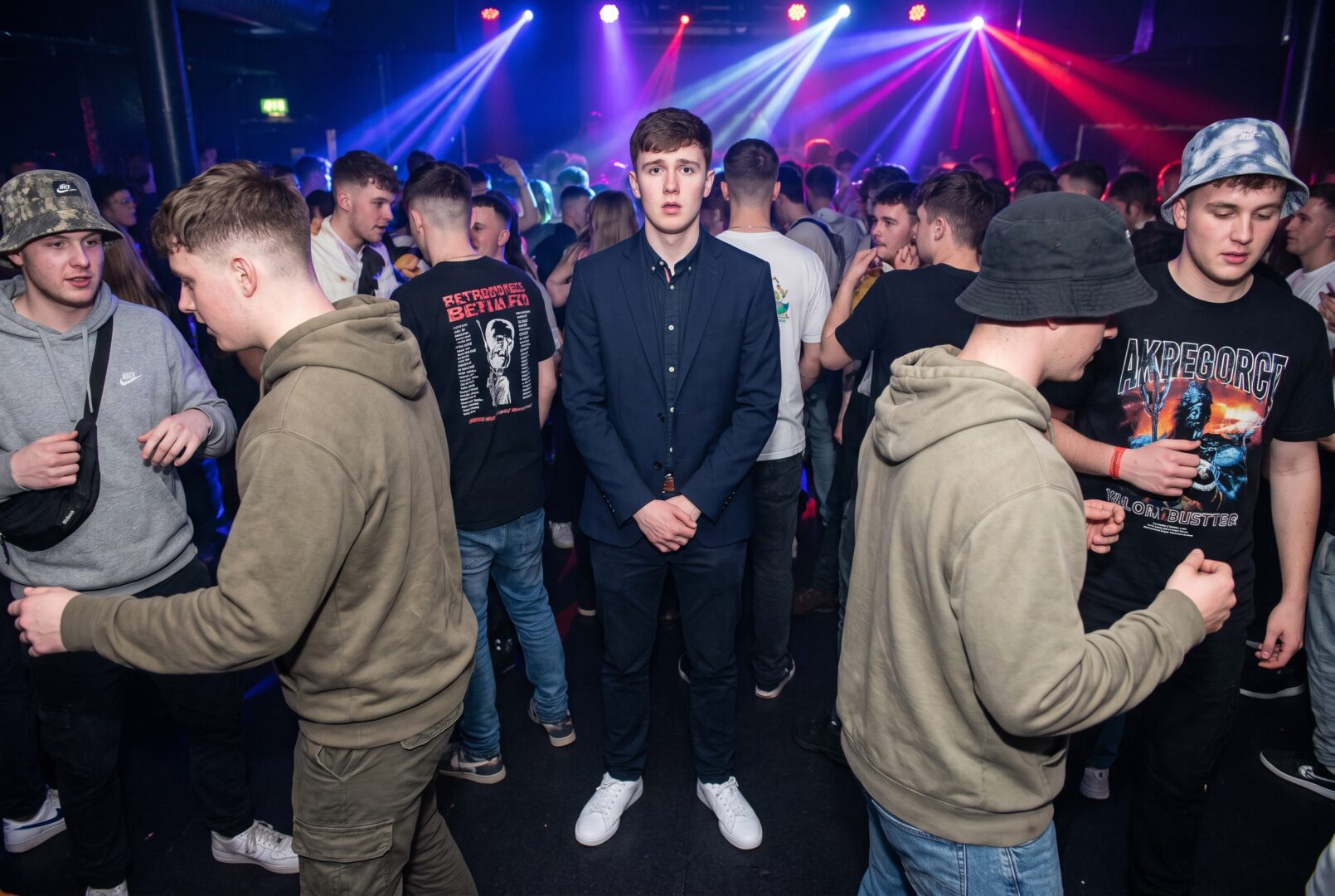 Overdressed man in a blazer and white sneakers looking out of place at a rave