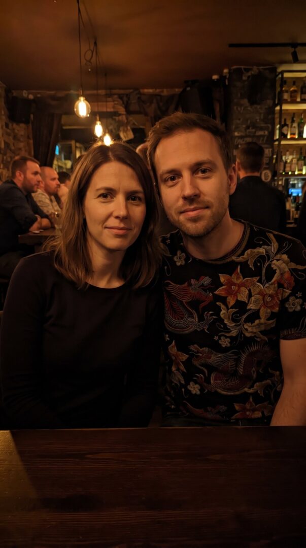 Couple at a warm-lit bar before a show, one in a dragon all-over-print t-shirt